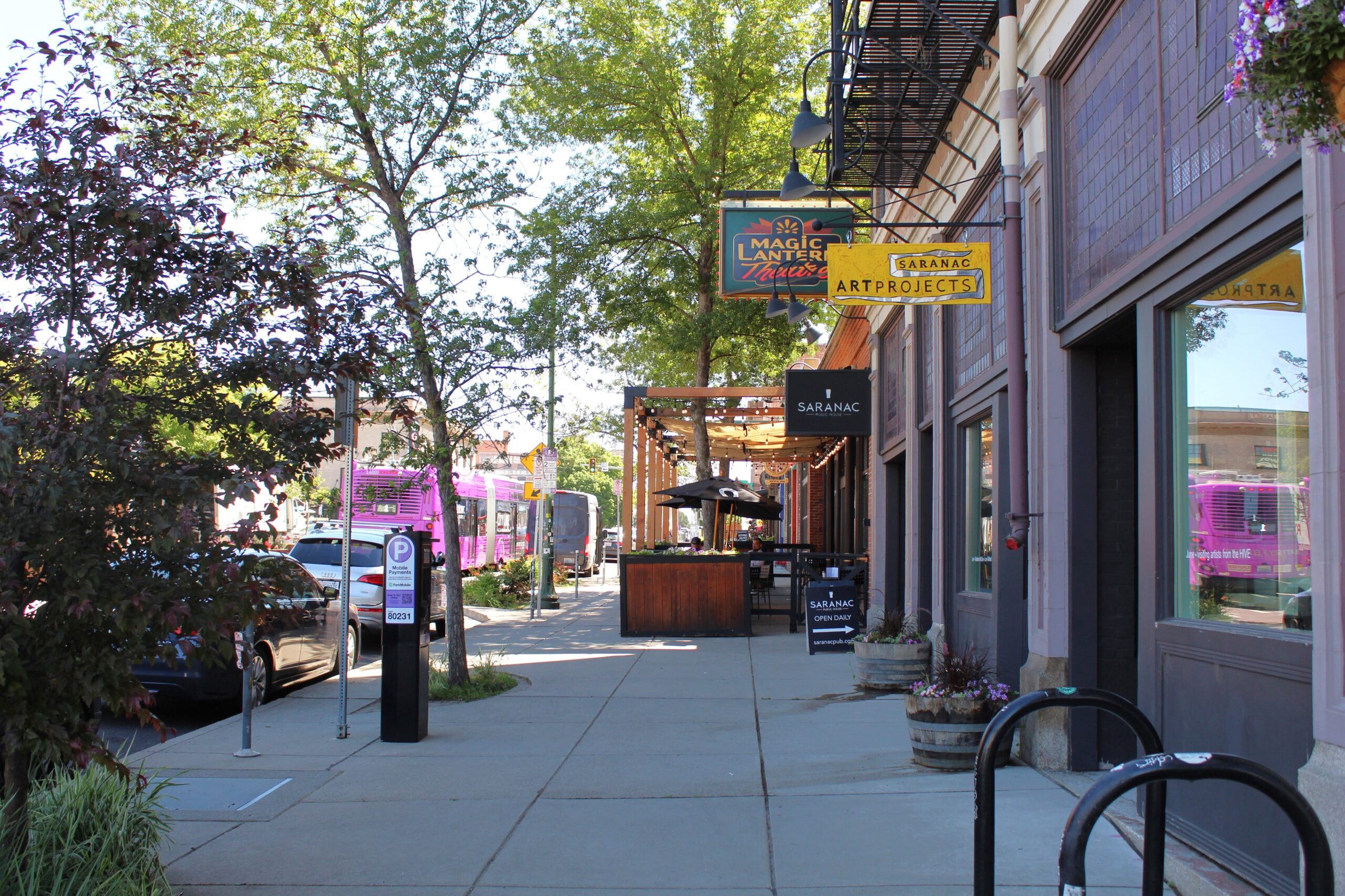 Streetscape of the Saranac Commons in Spokane. A pink CityLine bus runs in the background and small business signs hang in the foreground.